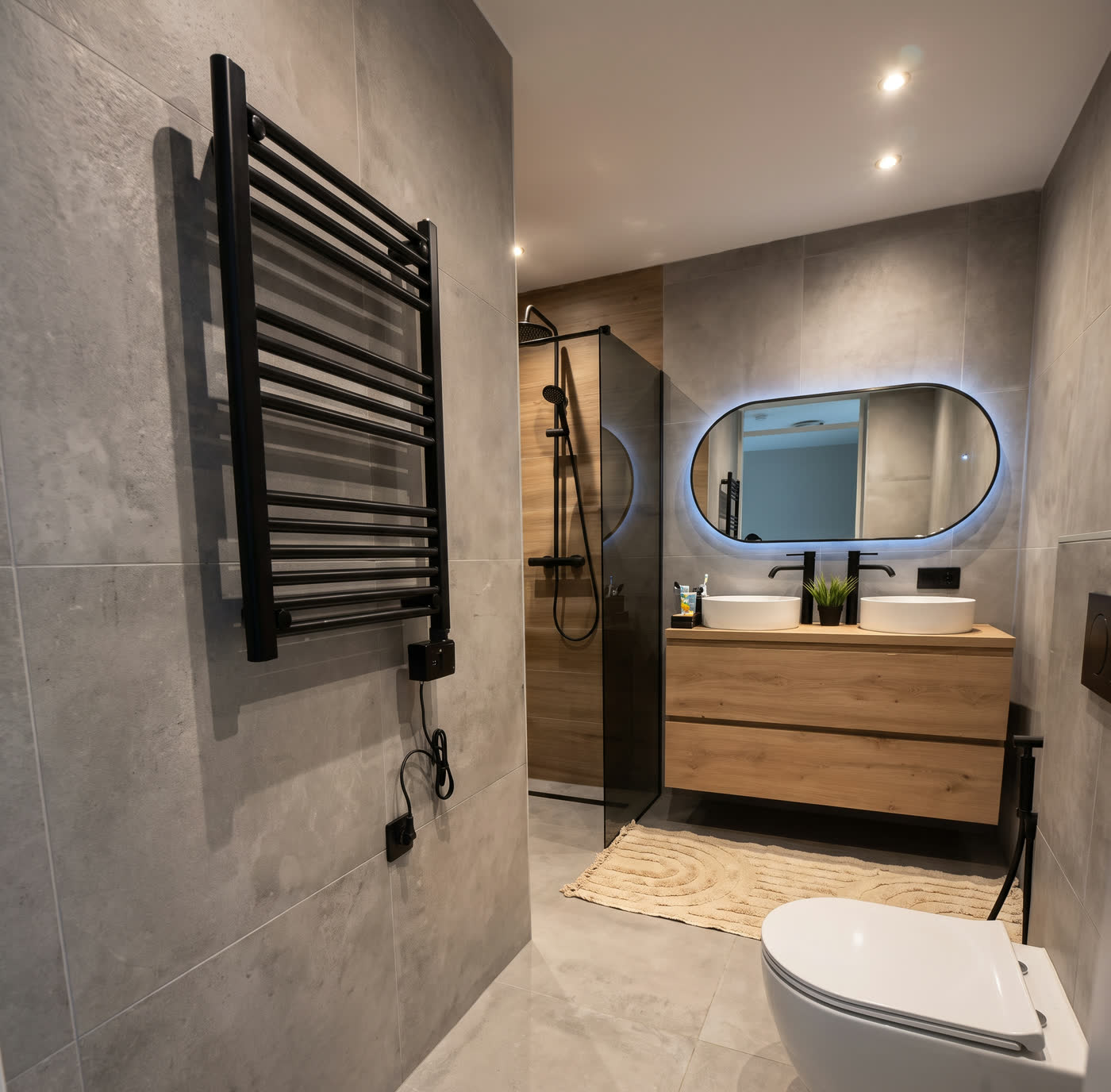 Opgeleverde badkamer met zwarte radiator, houten wastafelmeubel en verlichte spiegel