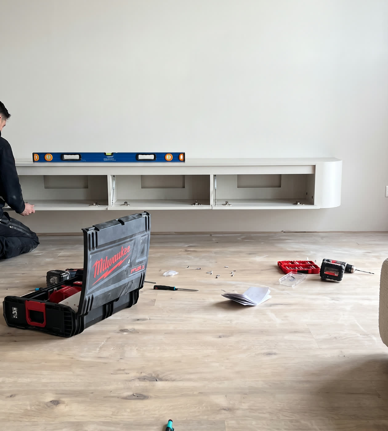 Zwevend wandmeubel wordt waterpas aan de muur gemonteerd, met waterpas en gereedschapskoffer op de vloer